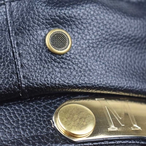 Dettaglio della trama in pelle PU nera con logo M in ottone e occhielli di ventilazione