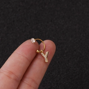 Gros plan d'une boucle d'oreille en U dorée avec pendentif lettre Y en zircon sur un doigt