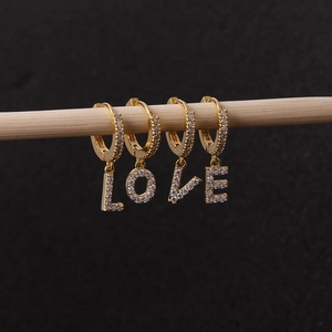 Gold zircon earrings set featuring LOVE letter pendants hanging on a wood branch