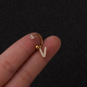 Détail macro d'un piercing hélix doré avec pendentif lettre V brillant en zircon