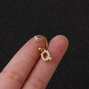 Macro d'une boucle d'oreille cartilage en acier doré avec pendentif lettre Q et zircone