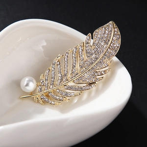 Elegant gold feather brooch with crystals and white pearl on white ceramic tray