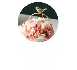 Close-up of golden bird metal ornament paired with pink hydrangea in a white ceramic pot