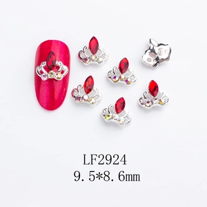 Macro shot of silver crown nail charms with red diamonds on a red fake nail