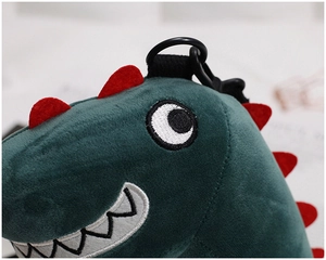 Close-up of green plush dinosaur charm with red spines, embroidery, and hook