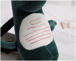 Close-up of soft green plush material with red linear embroidery on the dinosaur belly