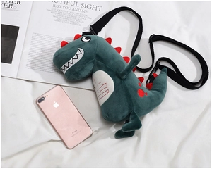 Detail of cute green plush dinosaur bag with red spikes beside a magazine and phone