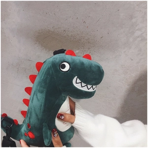 Detail of plush green dinosaur bag with red fins and adjustable black shoulder strap