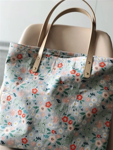 Detail of floral canvas tote bag showing leather handles and secure rivet attachment