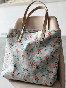 Detail of floral tote bag with daisy patterns and brown leather handle on a chair