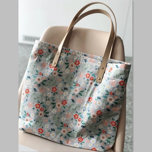 Detail of floral canvas tote bag with light blue print and brown leather handles