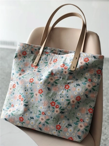 Close-up of floral canvas tote bag featuring khaki leather handles and metal rivets
