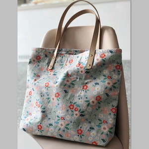 Large floral canvas tote bag in grey-blue with brown handles on a pink chair