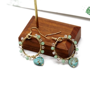 Detail of bohemian turquoise heart earrings with gold wire wrap and green beads on wood