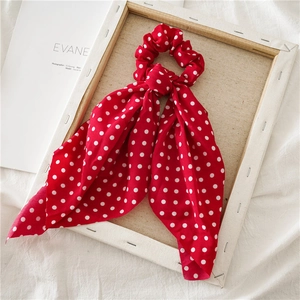 Dettaglio scrunchie rosso a pois con nastro lungo su una cornice di legno rustica
