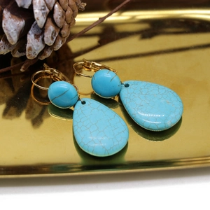 Detail of drop turquoise earrings with natural veins and golden metal hooks in a gold tray