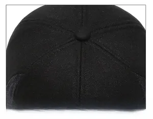 Close-up of the reinforced stitching and top button on a black wool winter baseball cap
