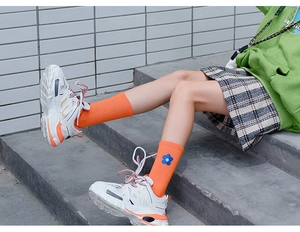 Detailed view of orange cotton socks with a small blue floral embroidery on the cuff