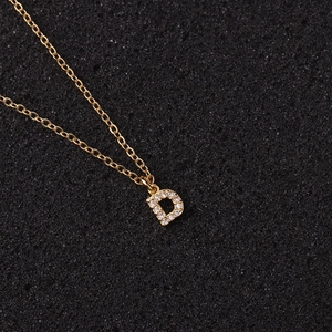 Macro detail of gold letter D pendant with small zircons on a delicate chain