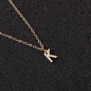 Detailed view of a gold-plated letter K pendant with sparkling zircon on a black background