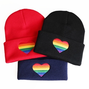 Detailed view of rainbow heart embroidery on red, black and navy knit beanies