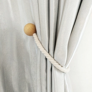 Detail of wooden magnetic curtain tieback with cotton rope on a grey curtain