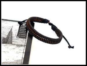 Close-up of hand-woven dark brown leather bracelet with fishbone pattern on a book