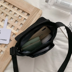 Black canvas messenger bag showing large capacity interior on white textured fabric