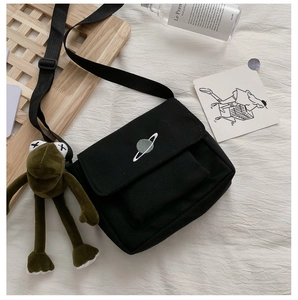 Detail shot of black canvas bag featuring planet embroidery and small frog pendant