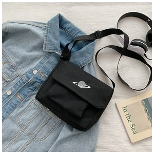 Detail of black canvas messenger bag featuring a white embroidered planet on textured fabric