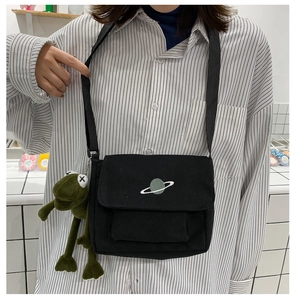 Detail of black canvas crossbody bag featuring planet embroidery and plush frog pendant