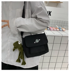 Detail of black canvas crossbody bag featuring star embroidery and green frog charm