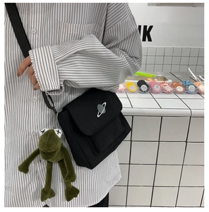 Detail of black canvas crossbody bag with planet embroidery and a cute frog plush charm