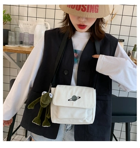 White canvas messenger bag with planet print and green frog plush charm detail