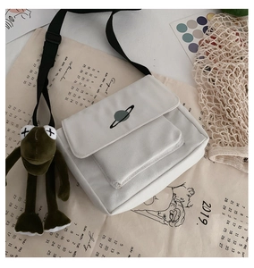 Flat lay of white canvas bag with planet print and green frog plush charm accessory