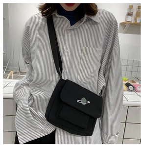 Detail of black canvas crossbody bag featuring a small planet embroidery and adjustable strap