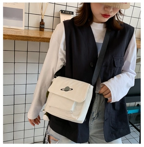 Detail view of beige canvas messenger bag featuring planet embroidery and black strap