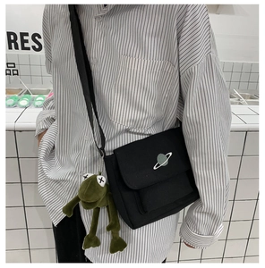 Detail of black canvas crossbody bag with planet embroidery and green frog charm