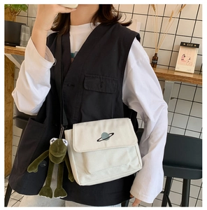 Detail of white canvas crossbody bag with planet embroidery and green frog plush charm
