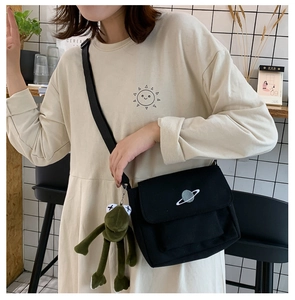Detail of black canvas messenger bag with planet embroidery and plush pendant