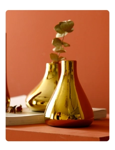 Detail of two golden ceramic vases with mirror finish on books against orange background
