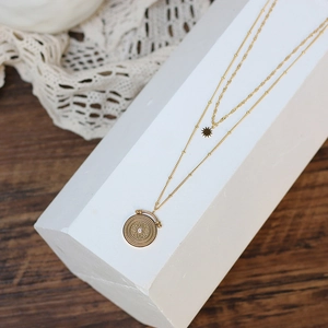 Detail of double-layered gold necklace with sunburst and mandala star pendants