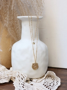 Close-up of gold double-layer necklace with sunburst coin pendant on ceramic vase