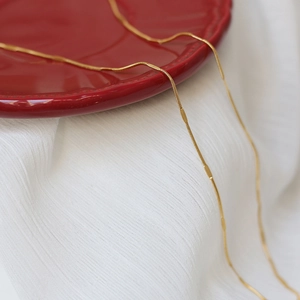 Close-up of a gold water wave chain necklace draped on elegant white fabric