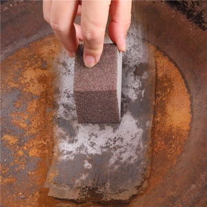 Brown carborundum sponge cleaning heavy rust and grime off a metal pot surface