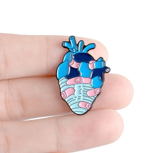 Close-up of a blue anatomical heart enamel pin with a pink bandage detail held in hand