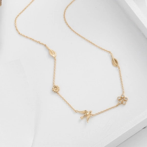 Detail of gold necklace featuring delicate leaf, flower, and bird charms with crystals