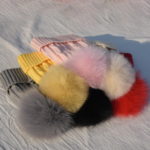 Detail view of colorful knitted hats with large faux fur pom-poms in a textured stack