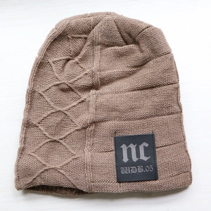 Detail of light coffee knitted beanie featuring vertical stripes and a black leather nc patch