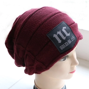 Close-up of burgundy knit beanie featuring premium black leather letter patch detail